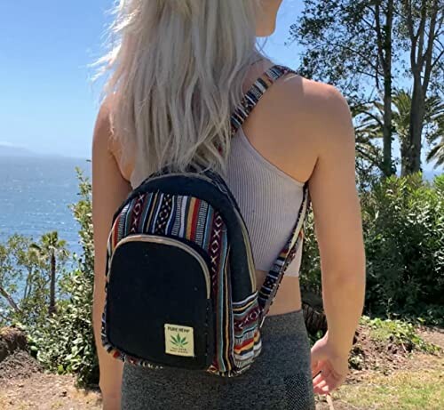 Woman wearing a colorful backpack standing outdoors near the sea.